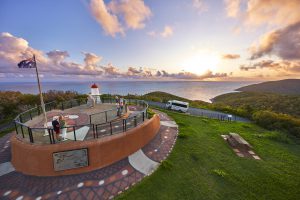 View from the top of Grassy Hill. People standing on lookout, grass surrounding and view out to the Coral Sea with sunny sky.
