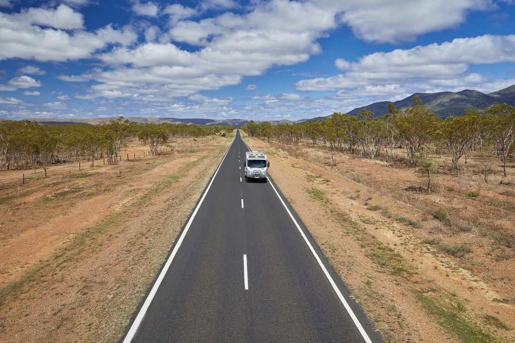 Small coach driving along straight road in the dry, dusty Australian Outback environment.