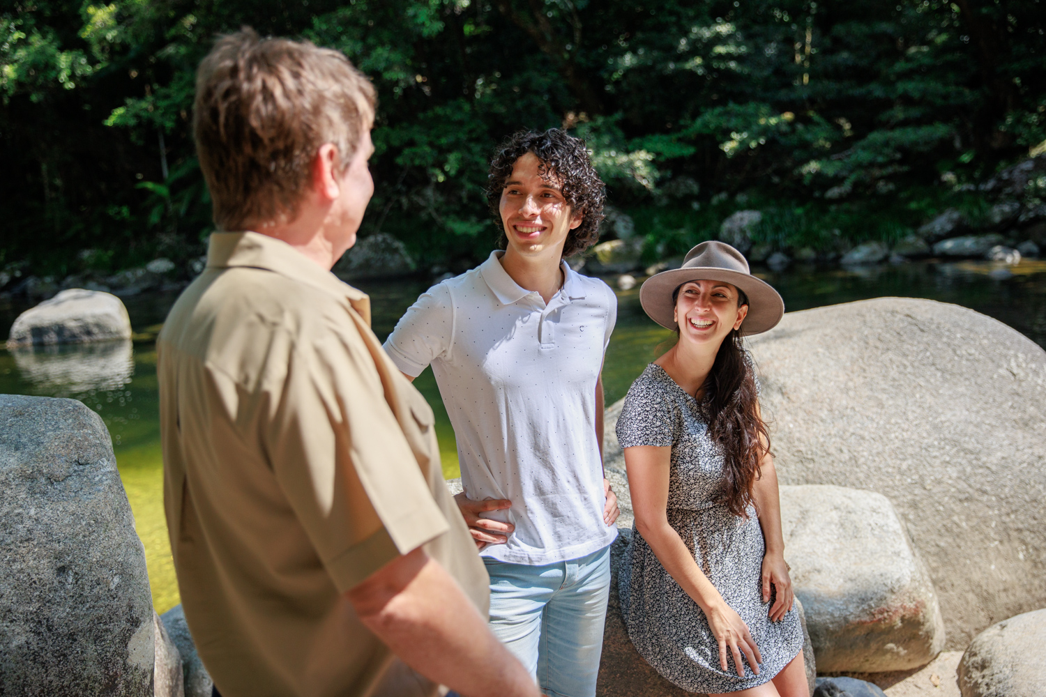 Young couple listening to a tour guide at Mossman Gorge with rainforest and river in the background.