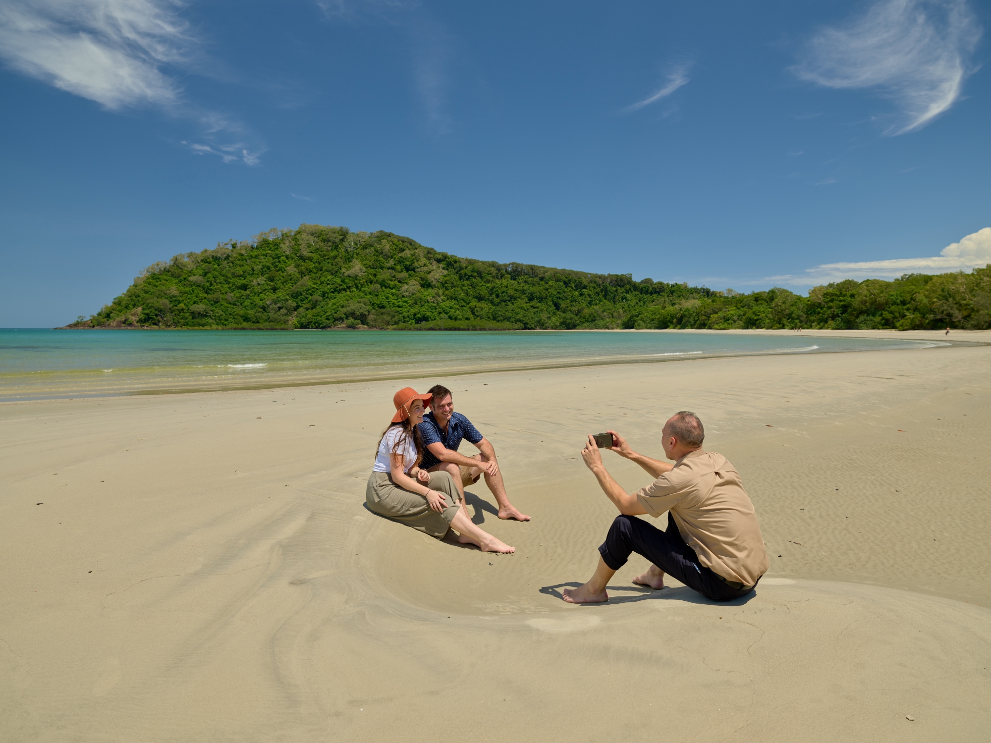 Couple sitting on Cape Tribulation beach with tour guide taking their picture